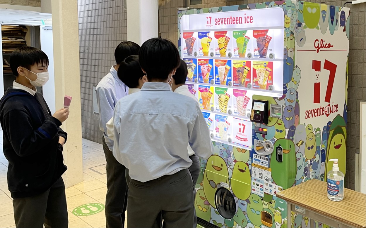 画像：セブンティーンアイスの自動販売機と、その前に集まる生徒たち